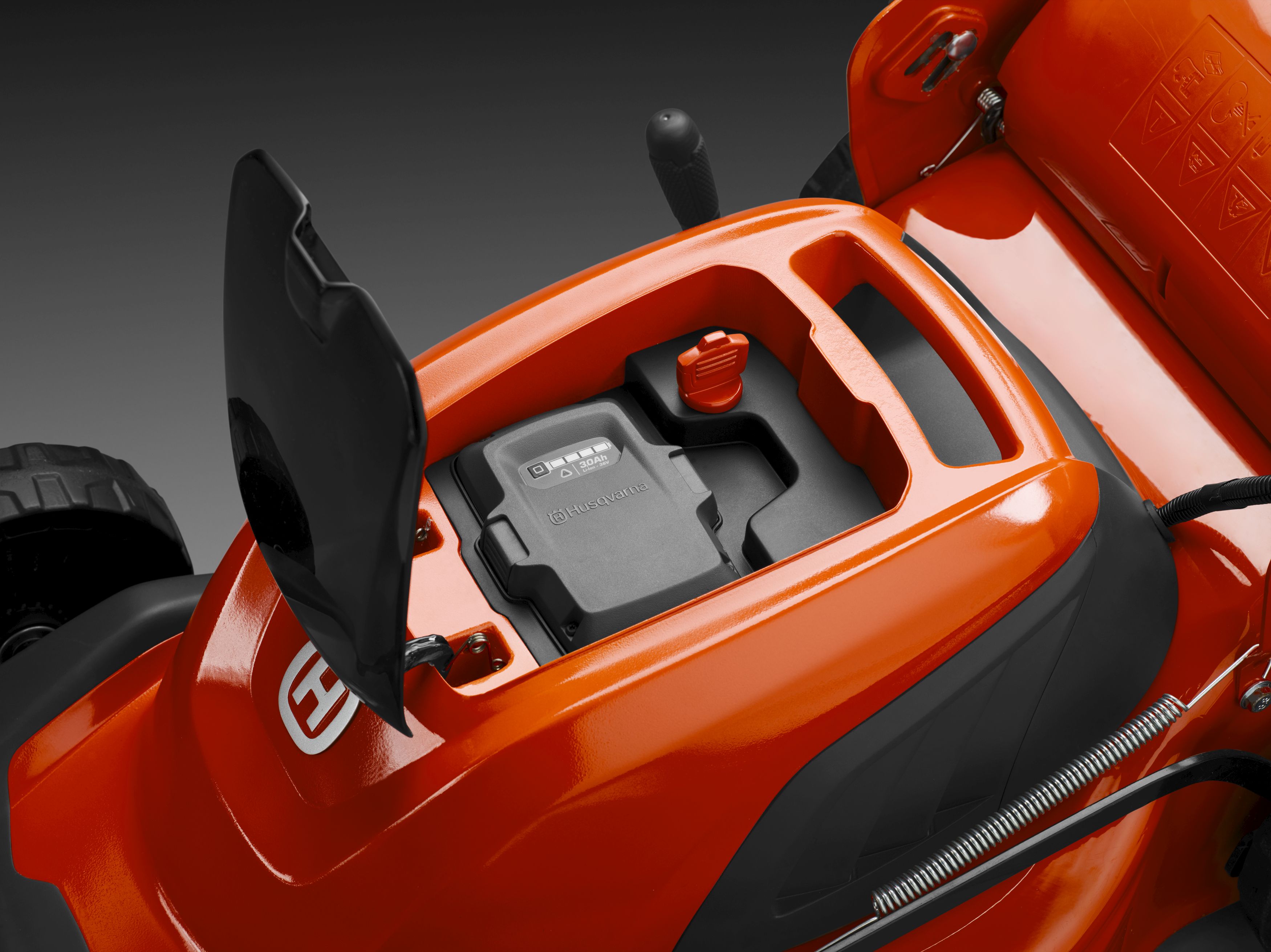 Zāles pļāvēja motors ar atvērtu pārsegu un bateriju iekšpusē.